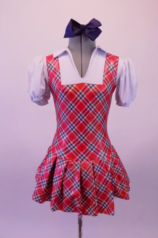 Red white and navy tartan school girl pinafore style costume has an attached pleated skirt and faux white blouse with pouffe sleeves and attached panty. Comes with large navy hair bow. Front
