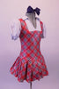 Red white and navy tartan school girl pinafore style costume has an attached pleated skirt and faux white blouse with pouffe sleeves and attached panty. Comes with large navy hair bow. Side