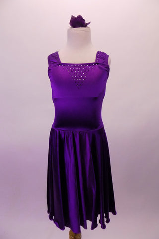Stretch satin tank style purple dress has a wide shoulder strap. The bodice has a series of colour matched crystals in a large triangular shape and along the straps. Comes with matching floral hair accessory. Front