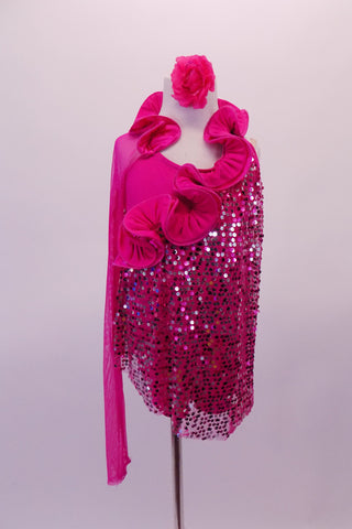 Fuchsia tunic style dress has a single long mesh sleeve and a curly ruffle collar that extends from the right shoulder, around the back of the neck and across the front of the torso at an angle. A sequined mesh tunic extends asymmetrically from below the ruffle. Comes with a floral hair accessory. Front