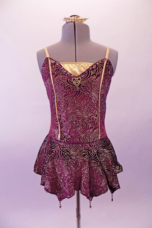 Merlot coloured leotard dress is velvet with gold swirl designs design, gold center inlay faux boning as well as a gold heart jewel at the bust. The short skirt has slight peaks with gold bead dangle accents. Comes with gold hair barrette. Front