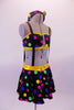 Black & colourful polka dot costume has a bandeau top and short circle skirt attached by elastic suspender bands to create a single piece. The waistband is yellow and there is a large tie-shaped crystal brooch accent attached to the front of the bandeau top. Comes with a matching bobbled headband. Side
