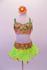 Orange and green two-piece beaded sequined costume has beaded sequin leaf accents along the neckline and waistband. The bottom has an attached lime green organza ruffled skirt with large dangling orange sequins accenting the edge. Comes with a large orange floral hair accessory. Front