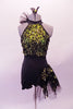 Short unitard is a halter style with a black short bottom. The top is a lime green with black sequined lace overlay. Two vertical straps extend from the back of the neck to support the back. There is a ruffled tulle accent at the left side of the neck that matches the ruffle accent at the left hip. Front