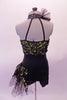 Short unitard is a halter style with a black short bottom. The top is a lime green with black sequined lace overlay. Two vertical straps extend from the back of the neck to support the back. There is a ruffled tulle accent at the left side of the neck that matches the ruffle accent at the left hip. Back