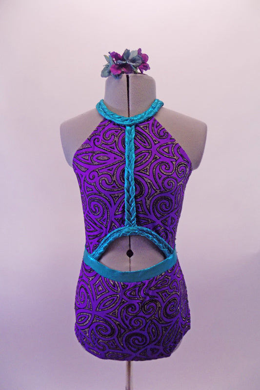 Purple and pewter leotard has an intricate swirl design throughout. The costume has a halter neck with an oval opening at the front center & completely open back. The bright splash of turquoise is evident in the braided banding that accents the front torso, collar, waist & neck straps. Comes with a floral accessory. Front