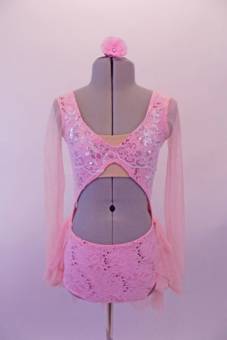 Pink sequined lace leotard dress has an open midriff in a unique shape. The bust comes together at the center but is reinforced with a nude bandeau beneath the bra, along the bustline. The open back has three straps that clip on the right side. Has attached flowy pink sheer skirt, long sleeves & pink hair accessory. Front