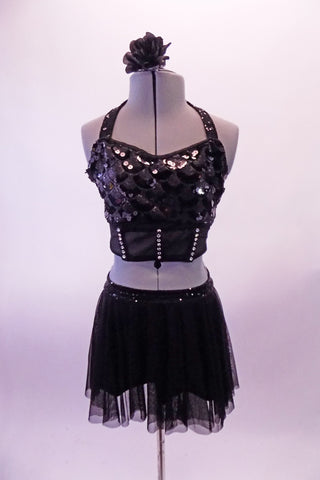 Two-piece black costume has a scale design front sequined haft top with halter neck, crystal accented under-bust band and crystal covered sheer back. The matching short sheer mesh skirt has sequined waistband and attached brief. Comes with a floral hair accessory. Front