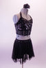 Two-piece black costume has a scale design front sequined haft top with halter neck, crystal accented under-bust band and crystal covered sheer back. The matching short sheer mesh skirt has sequined waistband and attached brief. Comes with a floral hair accessory. Back
