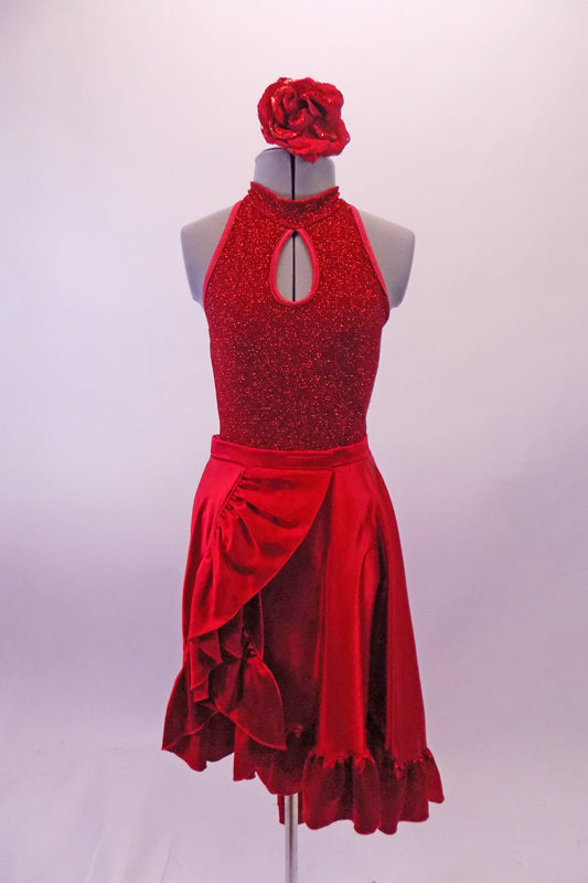 Two-piece costume has a glittery red halter neck leotard with front peek-a-boo loop at the chest. The open upper back had four thin vertical straps that join to the neck cuff. The accompanying red satin skirt is a wrap with large ruffle. The skirt opens at the side and is reinforced by two velcro bands. Has red flower. Front
