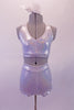 White shimmery two-piece costume has an iridescent colourful glow with a tone-on-tone animal print. The halter neck of the top leaves the back fully open. The bottom is a high waisted booty shorty with double banded legs for gold hold. Comes with a hair accessory. Front