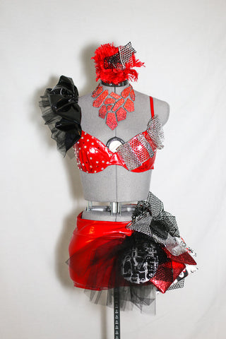 Red pleather 2 piece jazz costume with ruffle along the right shoulder. Shorts have a pouf-like attachment with foil,tulle and padded, decorative fabric pieces, front