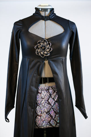 Long black leather-like coat  with large Swarovski broach accent. The coat is open in the front to reveal the snake-skin shorts. Zoom front