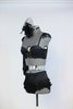 Black bustier style bra with fringed epaulets and gold chain details. at front. Has ruffled, high-waisted panty, long black gloves and a black head piece.Side